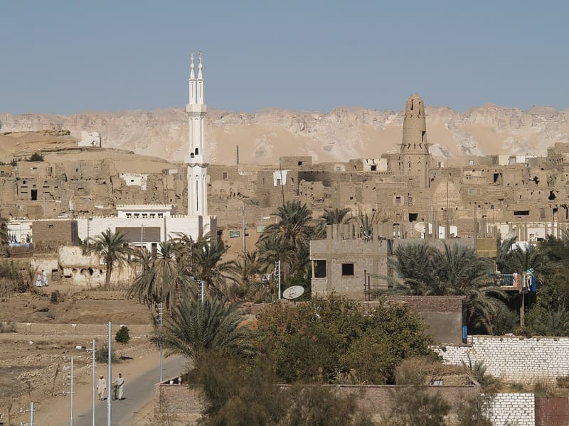 Il villaggio in mattoni crudi di Al-Qasr con minareti, palme e scarpata desertica