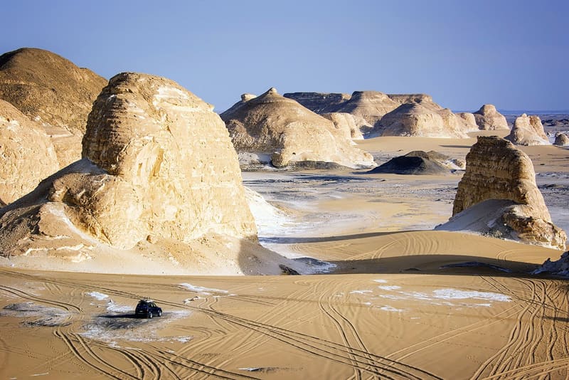 Panorama di grandi formazioni calcaree dorate e sabbia segnata dalle tracce dei fuoristrada