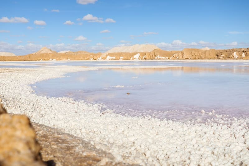 Riva incrostata di sale bianco lungo un lago salato dalle acque rosate a Siwa