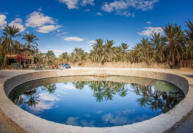 La sorgente circolare del Bagno di Cleopatra riflette palme e cielo azzurro a Siwa